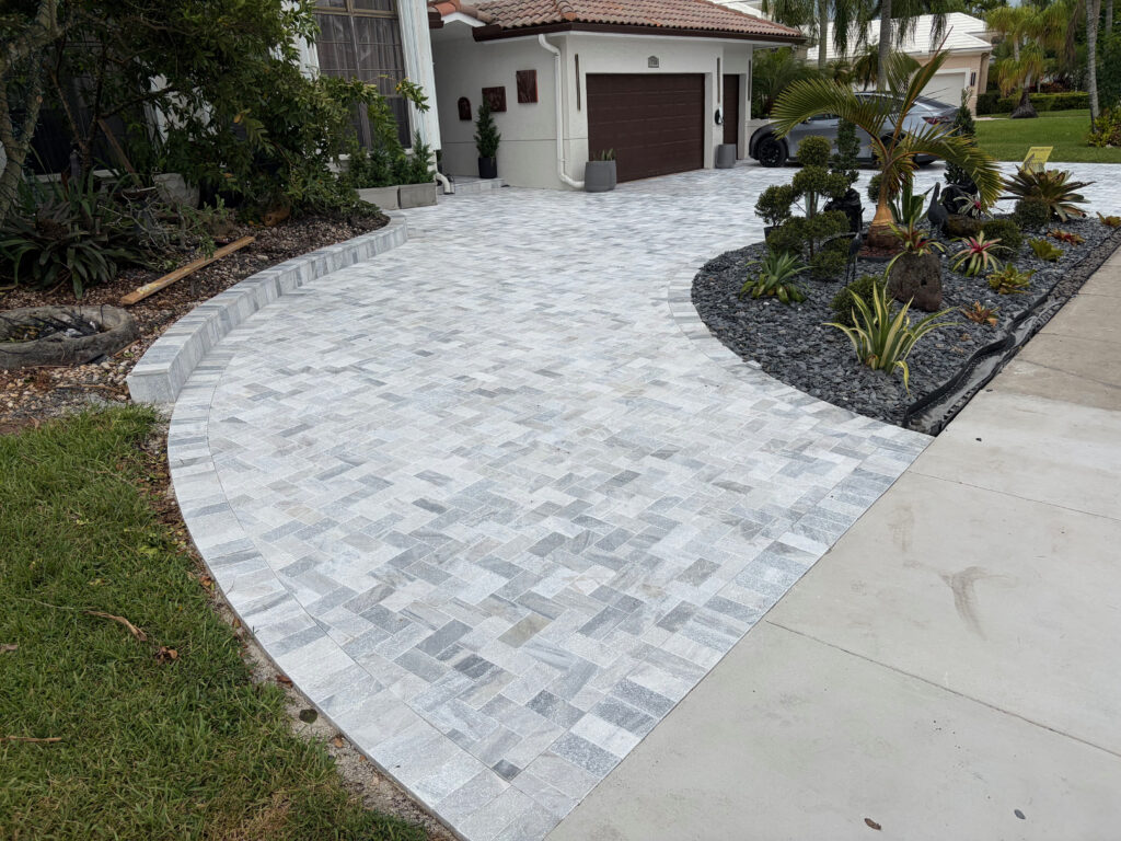 Curved gray and white stone driveway with a landscaped garden bed on the left and a two-car garage in the background